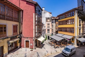 Une rue bordée d’immeubles, un café avec des tables en terrasse et un fourgon blanc garé sur le bord.
