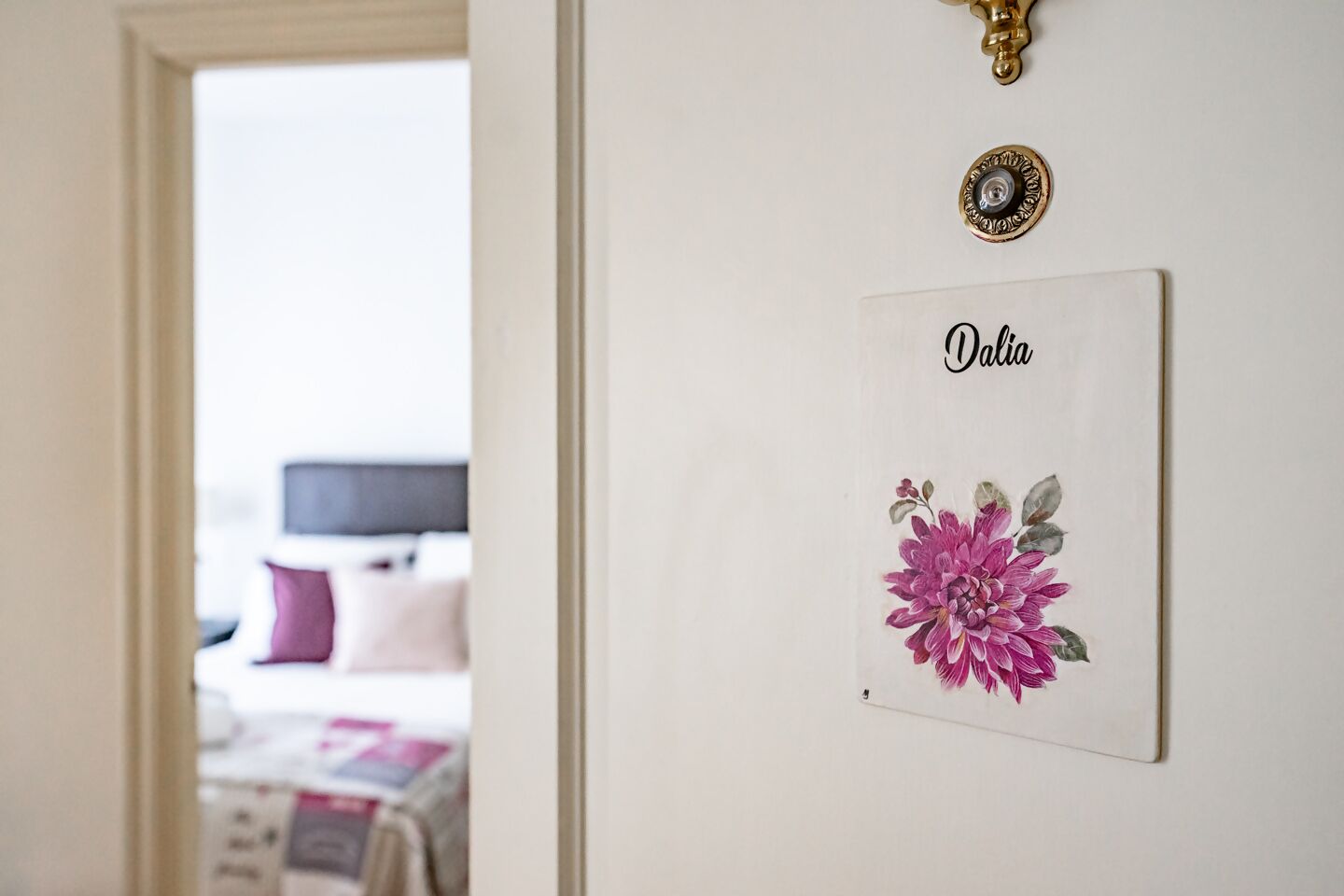 Una habitación con una puerta que da a otro espacio, una placa con el nombre 'Dalia' fijada en la pared, e impresión decorativa con motivos florales.