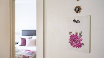 Una habitación con una puerta que da a otro espacio, una placa con el nombre 'Dalia' fijada en la pared, e impresión decorativa con motivos florales.