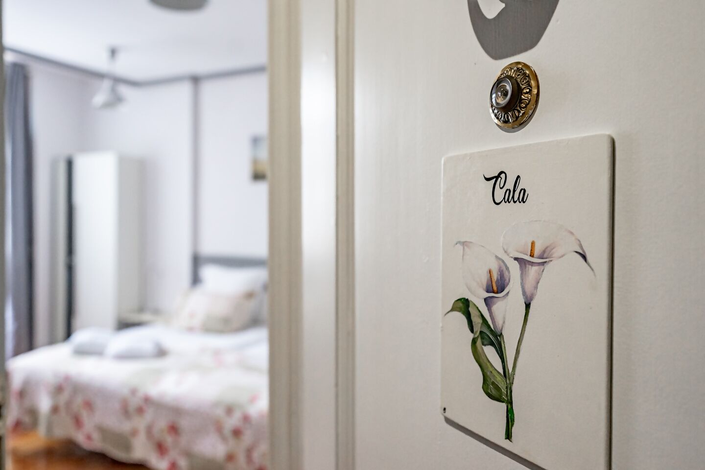 Une chambre d’hôtel avec un lit, une œuvre d’art représentant des callas accrochée au mur et une poignée de porte.