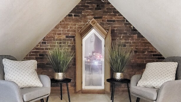 A cozy attic room with a sloped ceiling, two chairs with patterned cushions, and two potted plants.