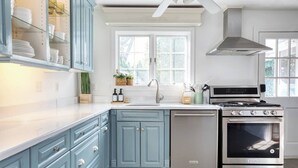 A kitchen with light blue cabinets, a stainless steel stove, and a window above the sink. - Peaceful Apartment with Waterview and Patio, Walk to Beach! (New Haven)