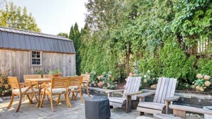 An outdoor patio area with wooden furniture, including a table and chairs, and a small shed in the background. - Peaceful Apartment with Waterview and Patio, Walk to Beach! (New Haven)