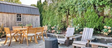 An outdoor patio area with wooden furniture, including a table and chairs, and a small shed in the background.
