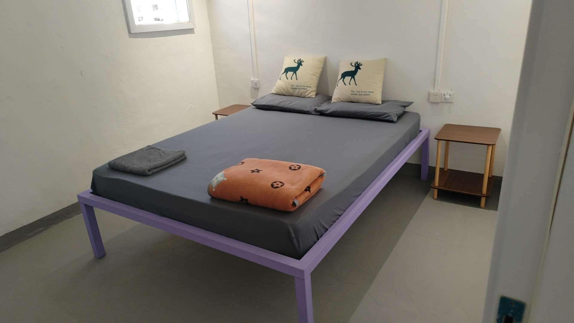 A single bed with a purple frame, grey bedding, and two pillows with deer designs.