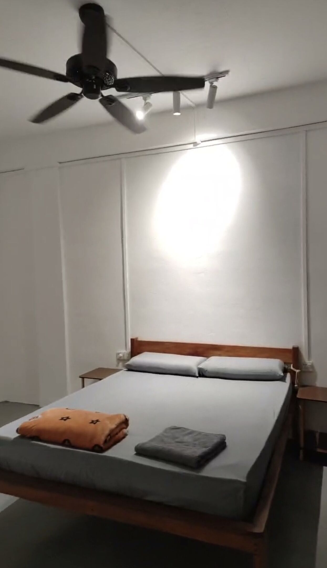 A bedroom with a bed, a ceiling fan, and a bedside table.