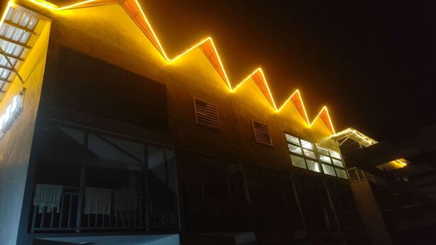 Um edifício com design de luz neon em zig-zag na fachada, grandes janelas e entrada visível.