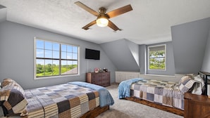A bedroom with two beds, a ceiling fan, a TV, and large windows with a view.