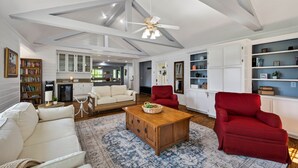 A spacious living room with a high ceiling, a wooden coffee table, a red armchair, and a white sofa.