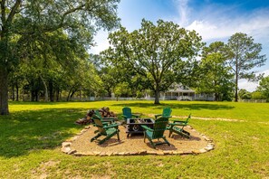 A patio with Adirondack chairs, a fire pit, and a stone fire ring. - Schulenburg Ranch Retreat, Private 27 Acres, Fishing, Game Room & Fire Pit (Schulenburg)