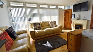 A living room with a sofa, a rug, a wooden cabinet, and a fireplace. - Chalet 72 is an elevated, single storey chalet on Kings Chalet Park, Cromer, in easy reach of Cromer (Cromer)