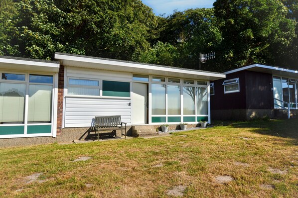 A row of single-story buildings with large windows, a bench, and a small garden area. - Chalet 72 is an elevated, single storey chalet on Kings Chalet Park, Cromer, in easy reach of Cromer (Cromer)