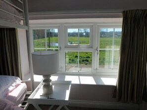 Una habitación con cama, una mesa con lámpara y vistas a un paisaje verde a través de amplios ventanales.