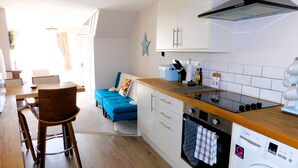 A compact kitchen with a washing machine, a dining area with a blue sofa, and a wooden dining table.