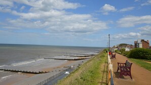 A coastal walkway with benches, a sea wall, and a clear sky.