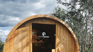 Una sauna de madera con diseño circular, un logotipo visible y una puerta.