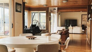 Amplia sala de estar con una gran mesa de comedor de madera, varias sillas, un sillón colgante y un televisor.