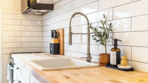 Une cuisine avec des carreaux de céramique blancs disposés en motif métro, un plan de travail en bois, un évier en acier inoxydable, une plante et un distributeur de savon.
