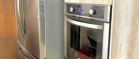 Uma cozinha com geladeira e forno de aço inoxidável, armários de madeira e micro-ondas embutido.