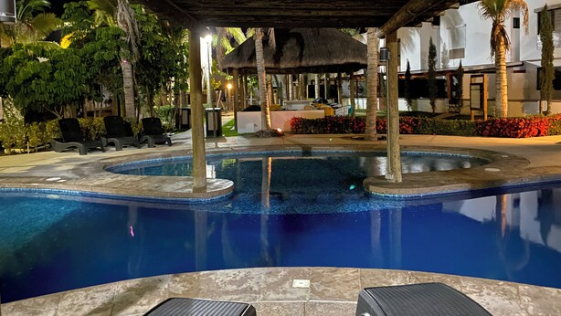 A swimming pool with a thatched roof structure, surrounded by palm trees and lounge chairs. - Palmilla Sunscape  (Mazatlán)