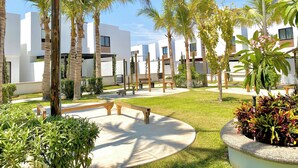 A courtyard with palm trees, benches, and a modern building with large windows. - Palmilla Sunscape  (Mazatlán)