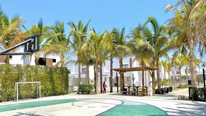 A basketball court with a green surface, surrounded by palm trees and a wooden pergola. - Palmilla Sunscape  (Mazatlán)