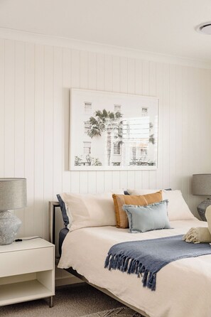 Une chambre à coucher avec un lit, des tables de chevet, un tableau accroché au mur et un luminaire au plafond.