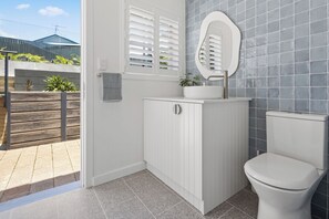 Une salle de bain avec un meuble-lavabo blanc, des toilettes et une fenêtre avec des volets.