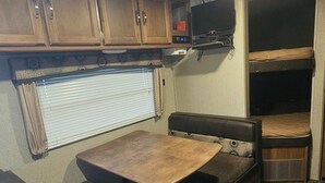 A compact RV interior with a kitchenette, a dining area, and a sleeping space.