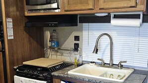 A compact kitchen with wooden cabinets, a microwave, a stove, a sink, and a small countertop area.