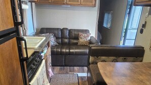 A compact RV kitchen with wooden cabinets, a stove, a sink, and a dining area with a bench.