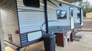 A recreational vehicle parked under a covered area with a table and chairs nearby.