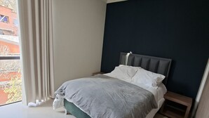 Een moderne slaapkamer met een bed, een nachtkastje en een raam met gordijnen.