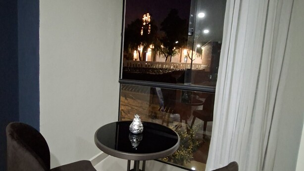 Een balkon met twee stoelen en een kleine tafel, met uitzicht op een verlicht gebouw in de nacht.