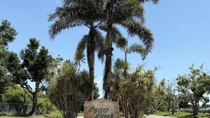 A sign reading "Oyster Creek" surrounded by palm trees and greenery. - Golf & Gulf – Pool Home Near Beach w/ Cart (Englewood)