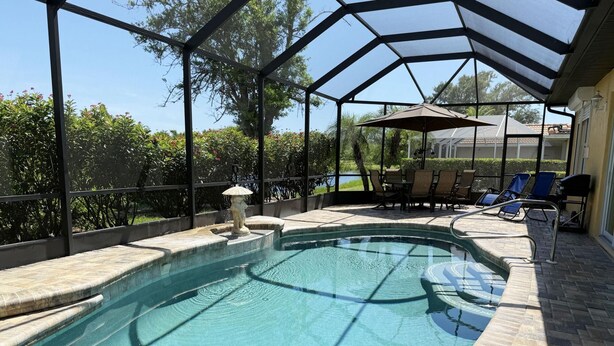 A pool with a glass enclosure, surrounded by lounge chairs and a small table. - Golf & Gulf – Pool Home Near Beach w/ Cart (Englewood)