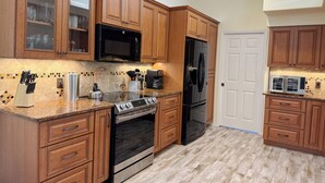 A kitchen with wooden cabinets, a stainless steel stove, a black refrigerator, and a microwave. - Golf & Gulf – Pool Home Near Beach w/ Cart (Englewood)