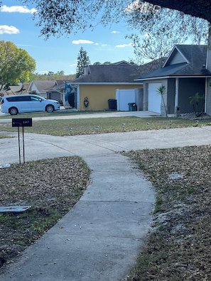 A residential driveway with a mailbox, a parked car, and houses in the background.