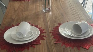 Ein Esstisch, gedeckt mit weißen Tellern, Tassen und einer klaren Vase mit roten und weißen Blumen.