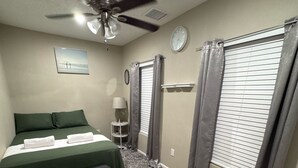 Ein Schlafzimmer mit Bett, Deckenventilator, einer Uhr und einem Fenster mit Vorhängen.