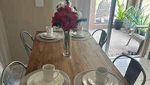 A dining table set with white plates and cups, a vase with red flowers, and chairs around the table. - Maxx Maximum Comfort LLC, 2-Bedrooms, 1 Bathroom (Winter Springs)