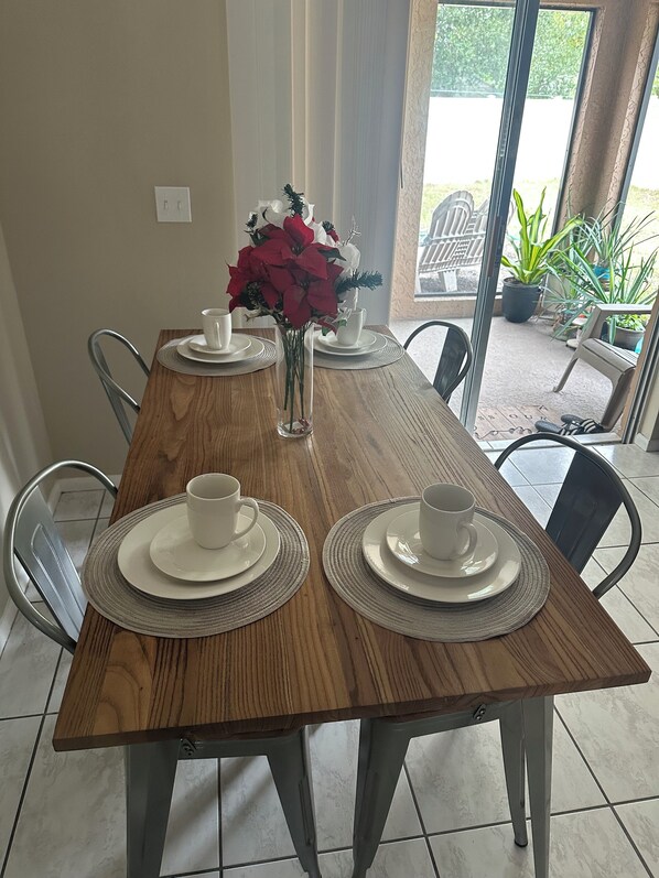 A dining table set with white plates and cups, a vase with red flowers, and chairs around the table.