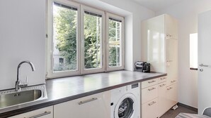 A modern kitchen with a built-in washing machine, a sink, and a window with a view of trees.