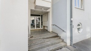 A building entrance with a sign reading "25 Withauergasse," a set of stone steps leading to a glass door, and a metal handrail on the right.