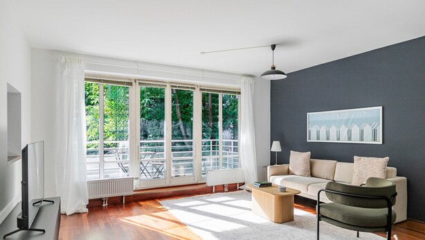 A modern living room with a large window, a sofa, a coffee table, and a TV.