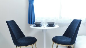 A room with two blue chairs, a white table, and a window with curtains. - Fontaine Kamata by Tranova (Tokyo)