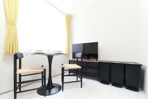 A modern room with a dining table, two chairs, a TV, and a black desk. - Fontaine Kamata by Tranova (Tokyo)