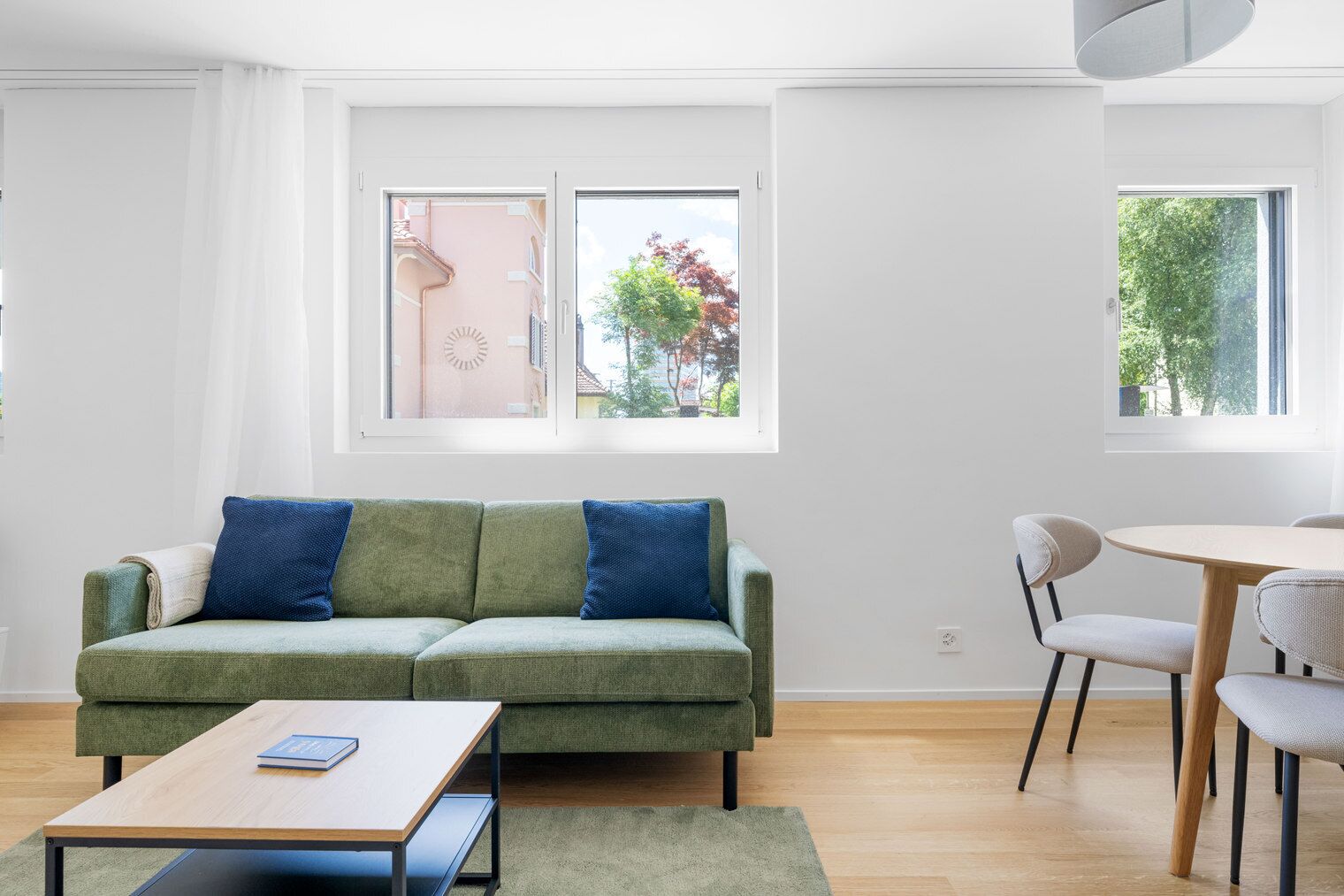A modern living room with a green sofa, two blue cushions, a wooden coffee table, and a dining area with a round table and chairs.