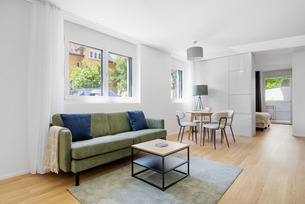 Een moderne woonkamer met een groene bank, een kleine tafel en een zithoek met stoelen.