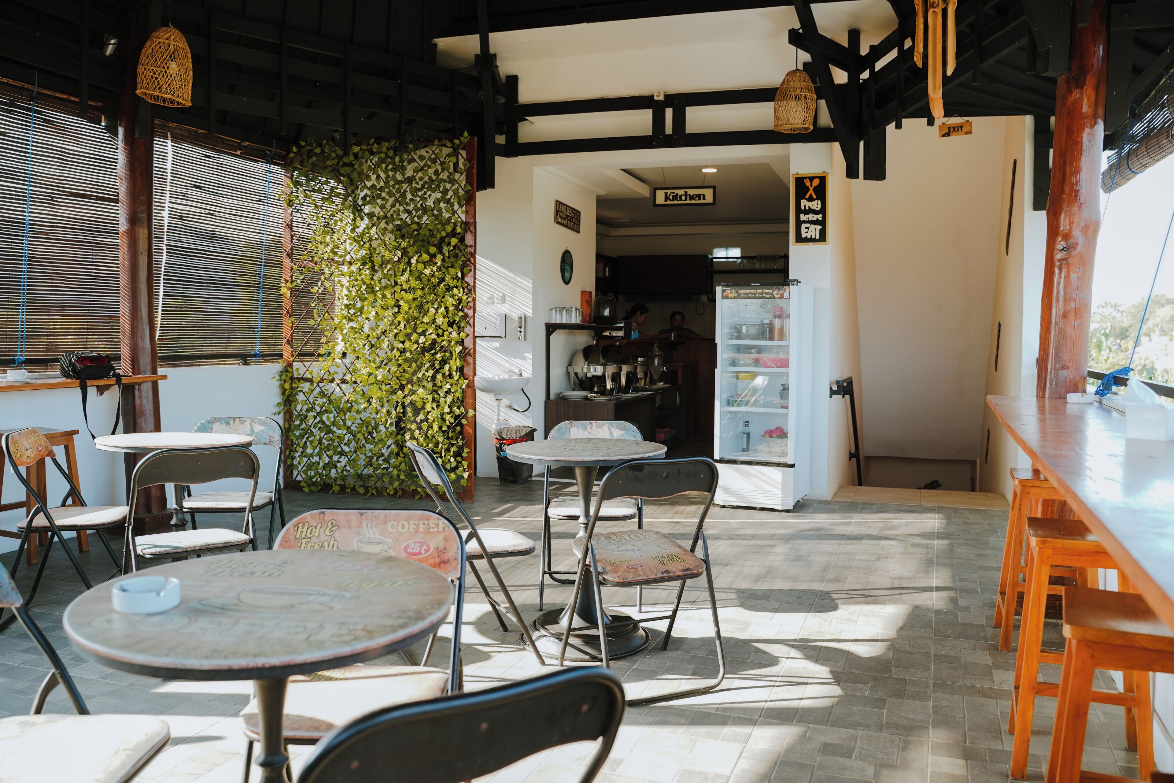 A cafe with tables and chairs, a kitchen area, and a view of the outdoors.